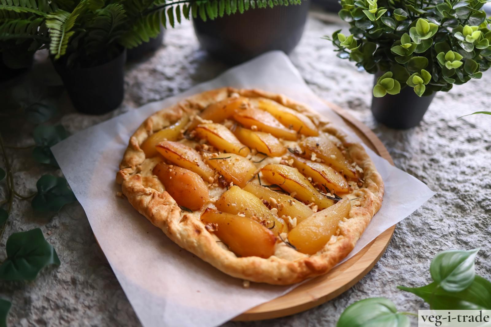Appetizing homemade rustic pear tart served on parchment paper, surrounded by fresh greens.