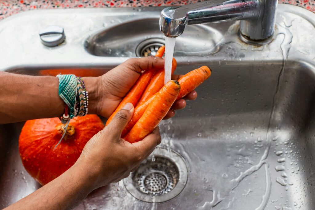 Persona lavando zanahorias bajo el grifo para lavar verduras correctamente